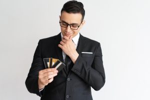 Young man in a suit looking thoughfully at a handful of credit cards.