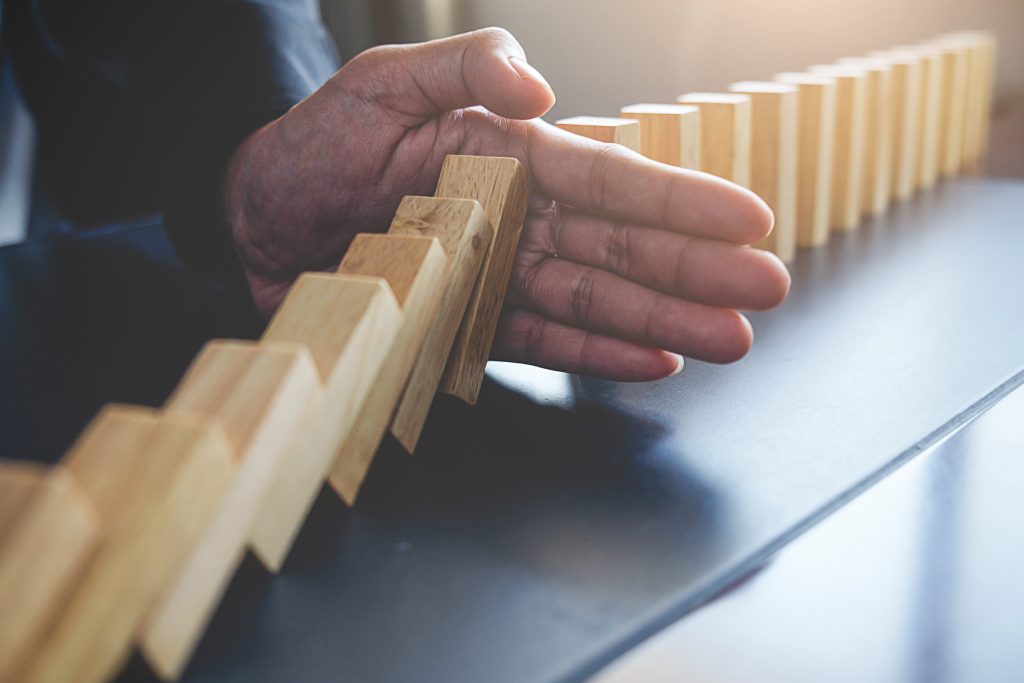 Dominoes falling into man's hand which keeps the dominoes behind his hand from falling.