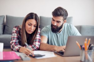 Woman and man sitting down with a computer, calculator, pen and paper working out their finances.